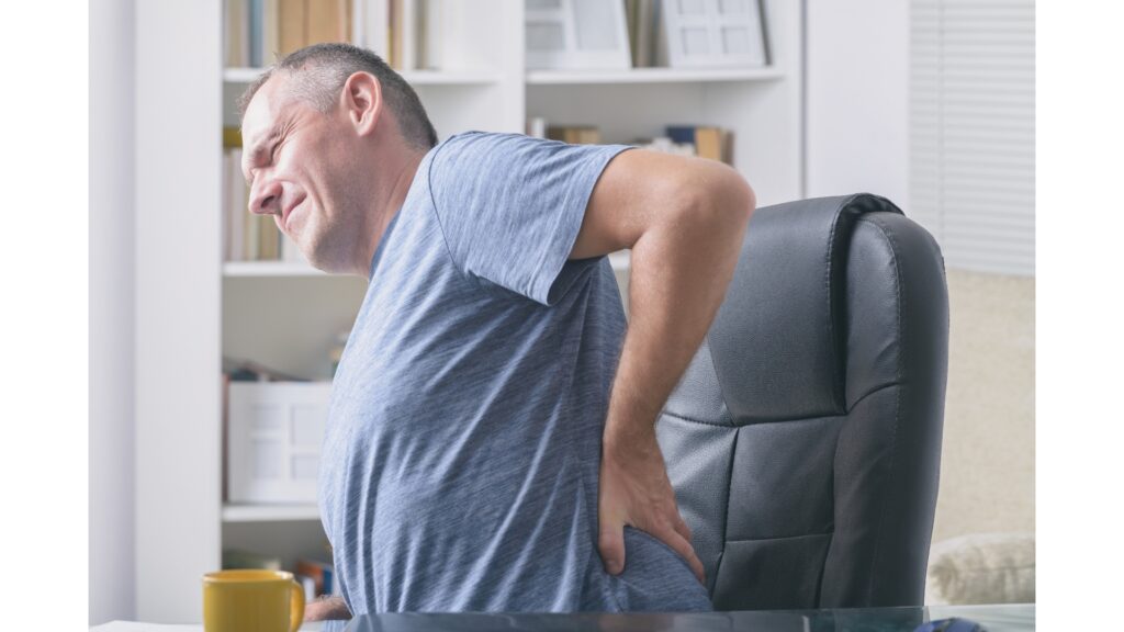 Man with low back pain sitting in a chair holding his back.